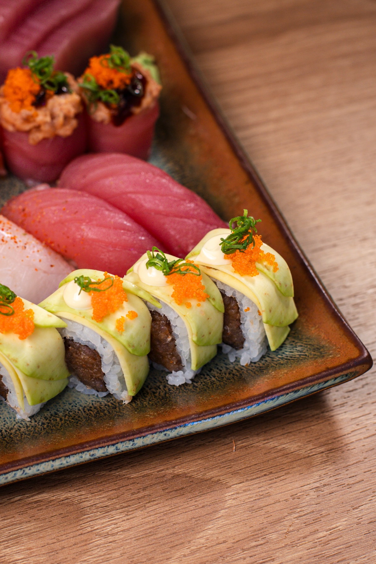 Hot roll com fatias de avocado, ovas alaranjadas e cebolinha ao lado de niguiris de atum em prato cerâmico