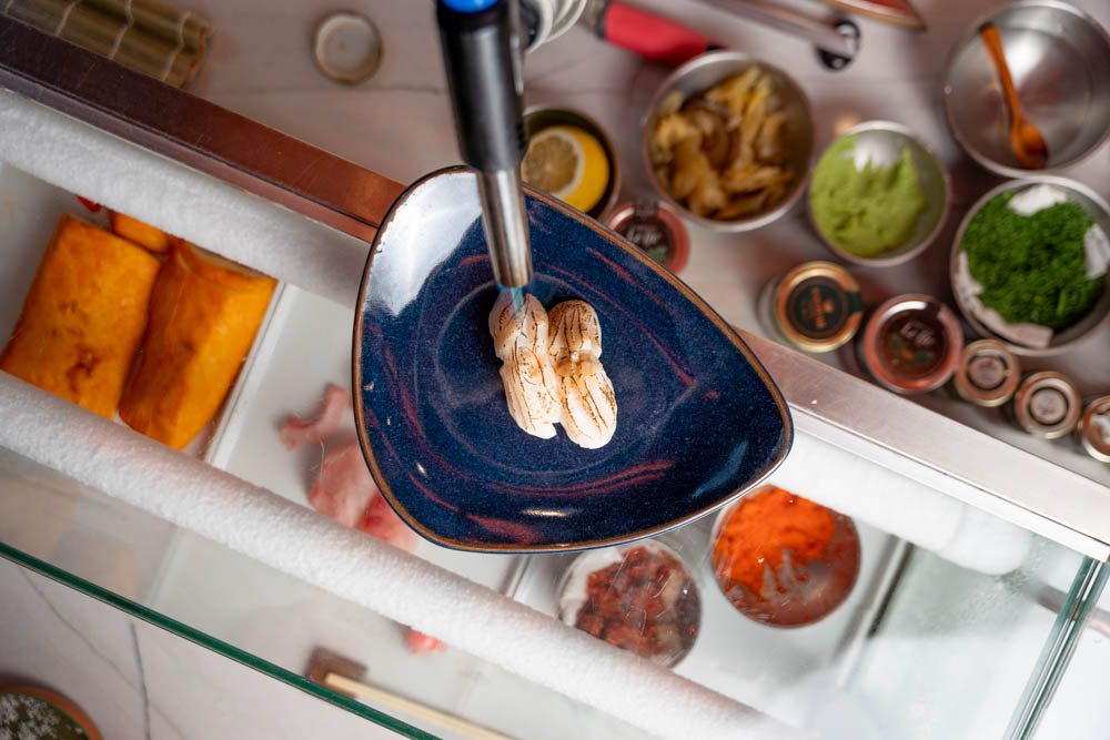 Maçarico finalizando peças em prato azul dentro da estação de trabalho do sushiman
