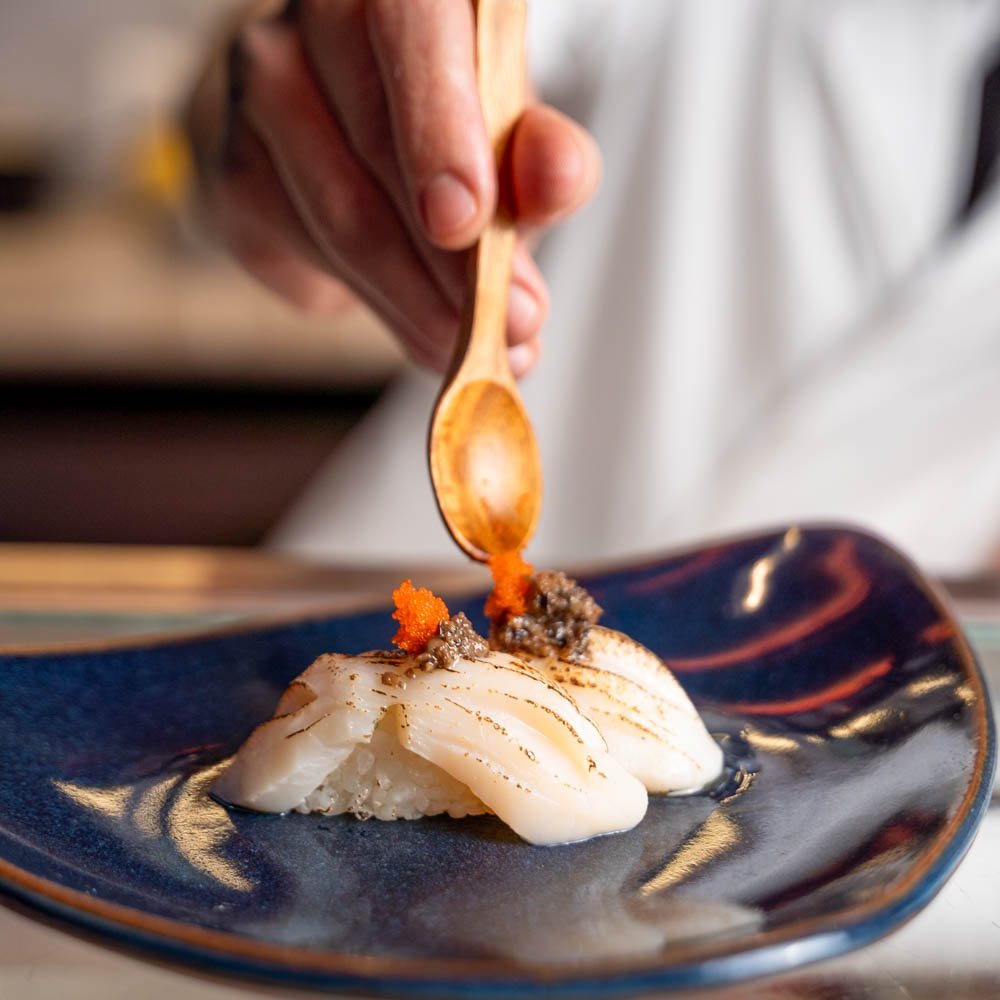 Chef finalizando niguiri maçaricado com colher de madeira sobre prato azul