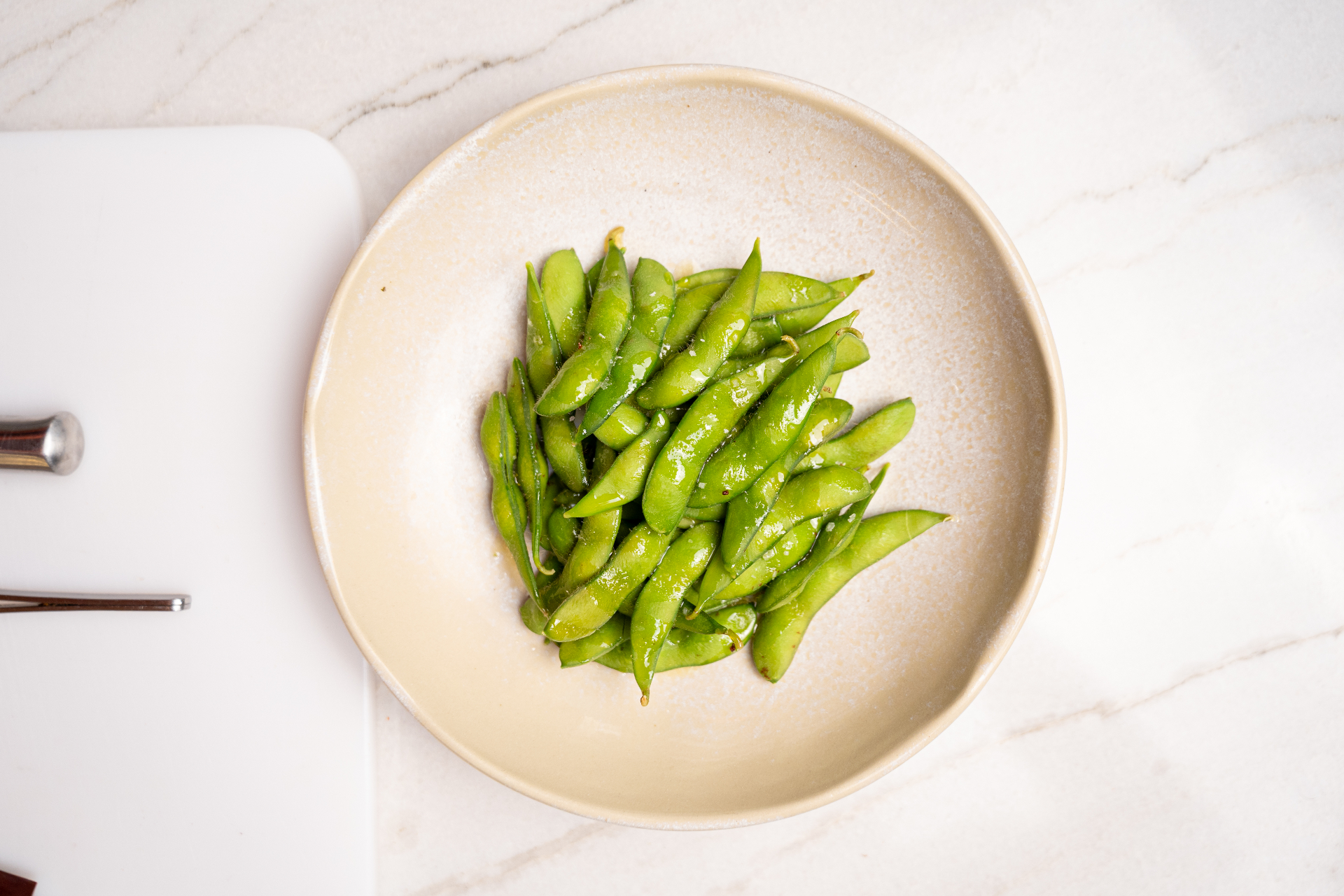 Bowl claro com edamame verde sobre superfície de mármore claro