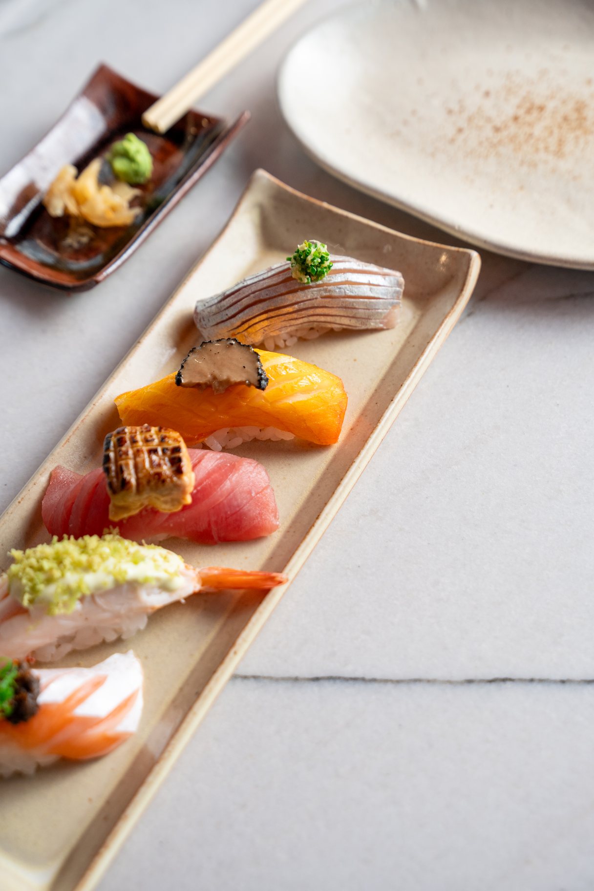 Prancha vertical com cinco niguiris premium finalizados com trufa, raspas e brasa